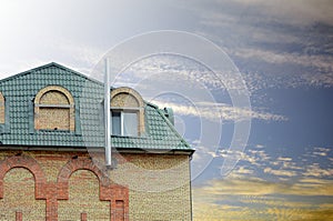 Metal roofing. Rain gutter on the roof top of house. Modern house with mansard windows against the blue sky. Chimney of building.