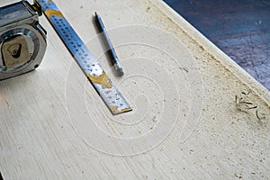 Metal ruler, carpenter`s pencil and measuring tape on the wooden plank. View in the workshop