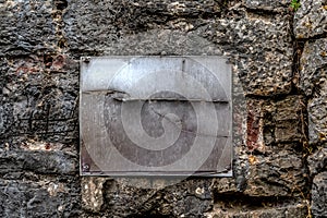 A metal rusty scratched blank plaque screwed with four screws to a stone wall
