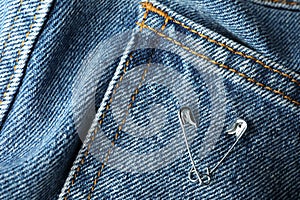 Metal safety pins on denim fabric, closeup