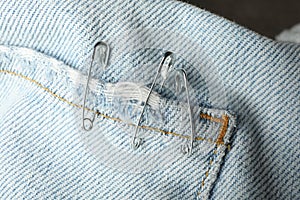 Metal safety pins on denim fabric, closeup