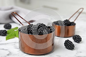 Metal saucepans with ripe blackberries on marble