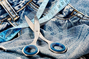 Metal scissors and blue measure tape on jeans. Tailors tools on denim textile, selective focus