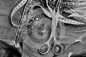 Metal scissors and yellow measure tape on jeans, close up