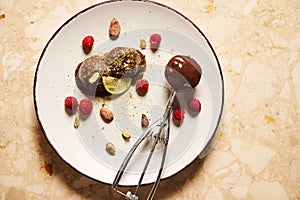 Metal scoop filled with dairy free chocolate sorbet, and frozen chocolate balls on white plate against marble background