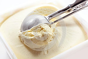 Metal scoop scrapes vanilla ice cream from the box, copy space