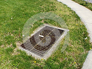 A metal sewer grate in the middle of a grass patch