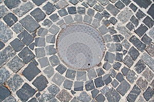 Metal sewer hatch on the stone pavement