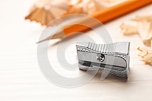 Metal sharpener near pencil and shavings on white wooden table, closeup. Space for text