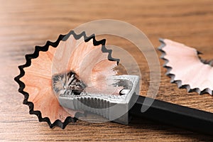 Metal sharpener with pencil shavings on wooden table, closeup