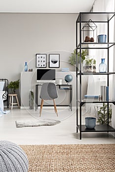 Metal shelf with cones, vases, plant and books in grey scandinavian home office with industrial desk with computer and copy space