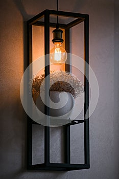 Metal shelf on a gray wall with a pot with dry herbs and a lamp