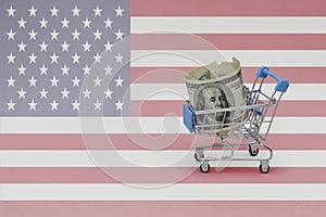 Metal shopping basket with dollar money banknote on the national flag of united states of america background. consumer basket