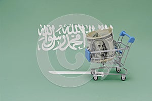 Metal shopping basket with dollar money banknote on the national flag of saudi arabia background. consumer basket concept. 3d