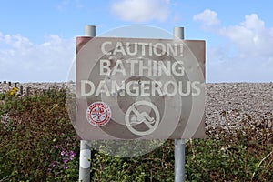 Metal sign at Bossington beach in Somerset warning that Bathing in the sea is dangerous. The sign is dented an looks as if it has