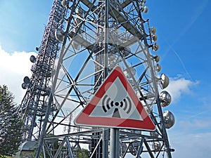 Metal sign with danger of electromagnetic waves. Group of towers for telecommunications, television broadcast, cellphone, radio