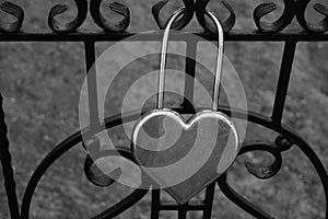 Metal silver door lock in the shape of a heart on the fence as a symbol of eternal love.