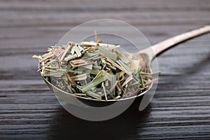 Metal spoon with aromatic dried lemongrass on wooden table, closeup