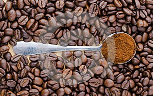 Metal spoon with ground coffee on table with coffee beans