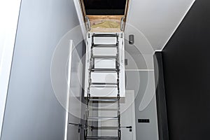 Metal stairs hidden in the ceiling to the attic with an opening hatch and folding stairs in the corridor, modern look.