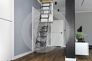 Metal stairs hidden in the ceiling to the attic with an opening hatch and folding stairs in the corridor, modern look.