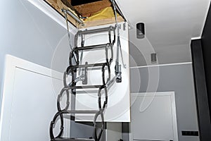 Metal stairs hidden in the ceiling to the attic with an opening hatch and folding stairs in the corridor, modern look.