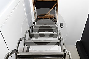 Metal stairs hidden in the ceiling to the attic with an opening hatch and folding stairs in the corridor, view from the bottom of