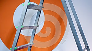 Metal stepladder against background of white-orange wall