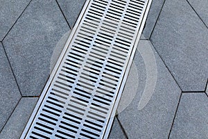 Metal storm sewer grate on shaped paving slabs in park. Drainage systems on paving slabs. Sidewalk construct.