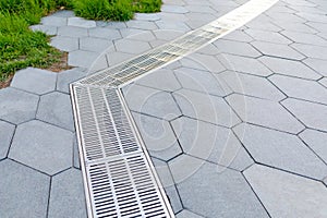 Metal storm sewer grate on shaped paving slabs in park. Drainage systems on paving slabs. Sidewalk construct. Selective