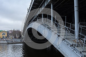 Metal structure of the bridge over city river. Stone coast of Moskva River