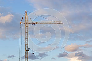 Metal structure construction crane on the background of the sunset sky with clouds