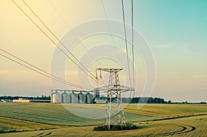 Metal support is a pillar of a high-voltage line in the field. Big elevator on the background. Industrialization of agriculture