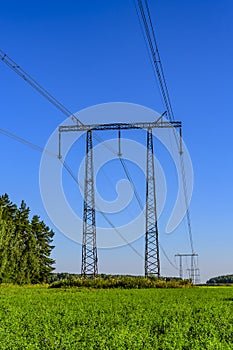 Metal supports and cables of a high-voltage transmission line over a green field in the early summer morning