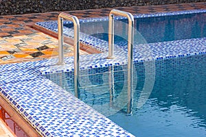 A metal swimming pool safe ladder (skimmer) on the entrance to the home inground poolside with the blue clean water.