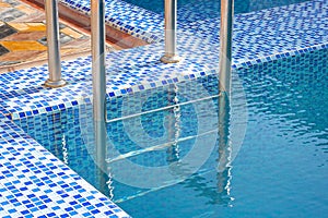 A metal swimming pool safe ladder (skimmer) on the entrance to the home inground poolside with the blue clean water