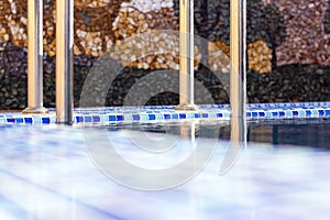 A metal swimming pool safe ladder (skimmer) on the entrance to the home inground poolside with the blue clean water