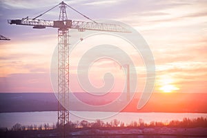 Metal tall construction crane on a background of orange sunset