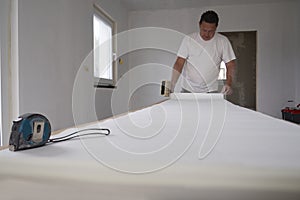 Metal tape measure on foreground,blurred smiling tanned man in white t-shirt with wide paint brush in hand.Copy space