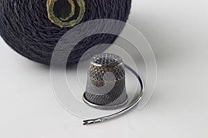 Metal thimble, sewing needle and spool of black thread on a white background