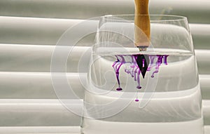 Metal tip of ink pen dipped in water. diffusion of blue ink in a transparent glass cup with clear water against the background of photo