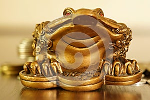 A metal toad next to a stack of coins. Symbol of happiness and financial success