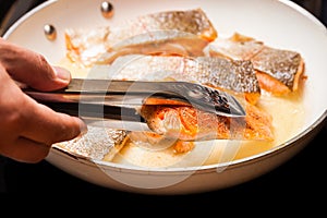 Metal tongs holding red trout fillet, also known as arctic char