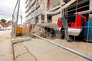 Metal trailer coupling of compressor peeks through wire fence on construction site