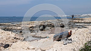 Metal trash on the rocky beach with fisherman and ship on the background. Sea pollution. Slow motion