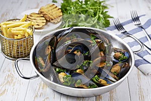 Metal tray with mussels cooked in sauce with garlic, parsley and lemon on a white wooden table