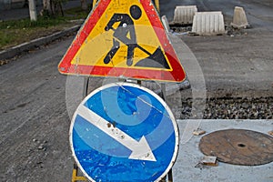 Metal tripod with attached  scratched signs of road works and detour, in connection with works on replacement of wells of heating