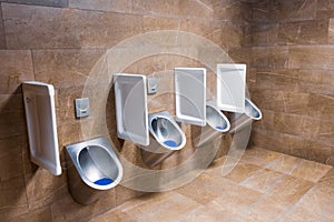 Metal urinals and one for children with an automatic sensor for flushing water after urinating. Men`s toilet in brown marble