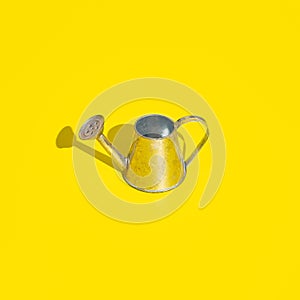 Metal watering can on bright yellow background. Minimal bold colored garden background. Gardening, growing, spring or summer