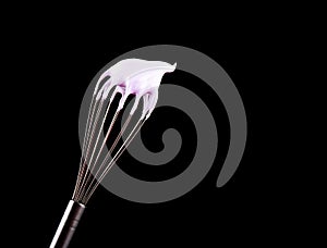 Metal whisk with pink cream isolated on black background. Clipping path.